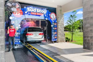 a minivan entering the vehicle entrance to a sud stop express car wash with an attendant watching